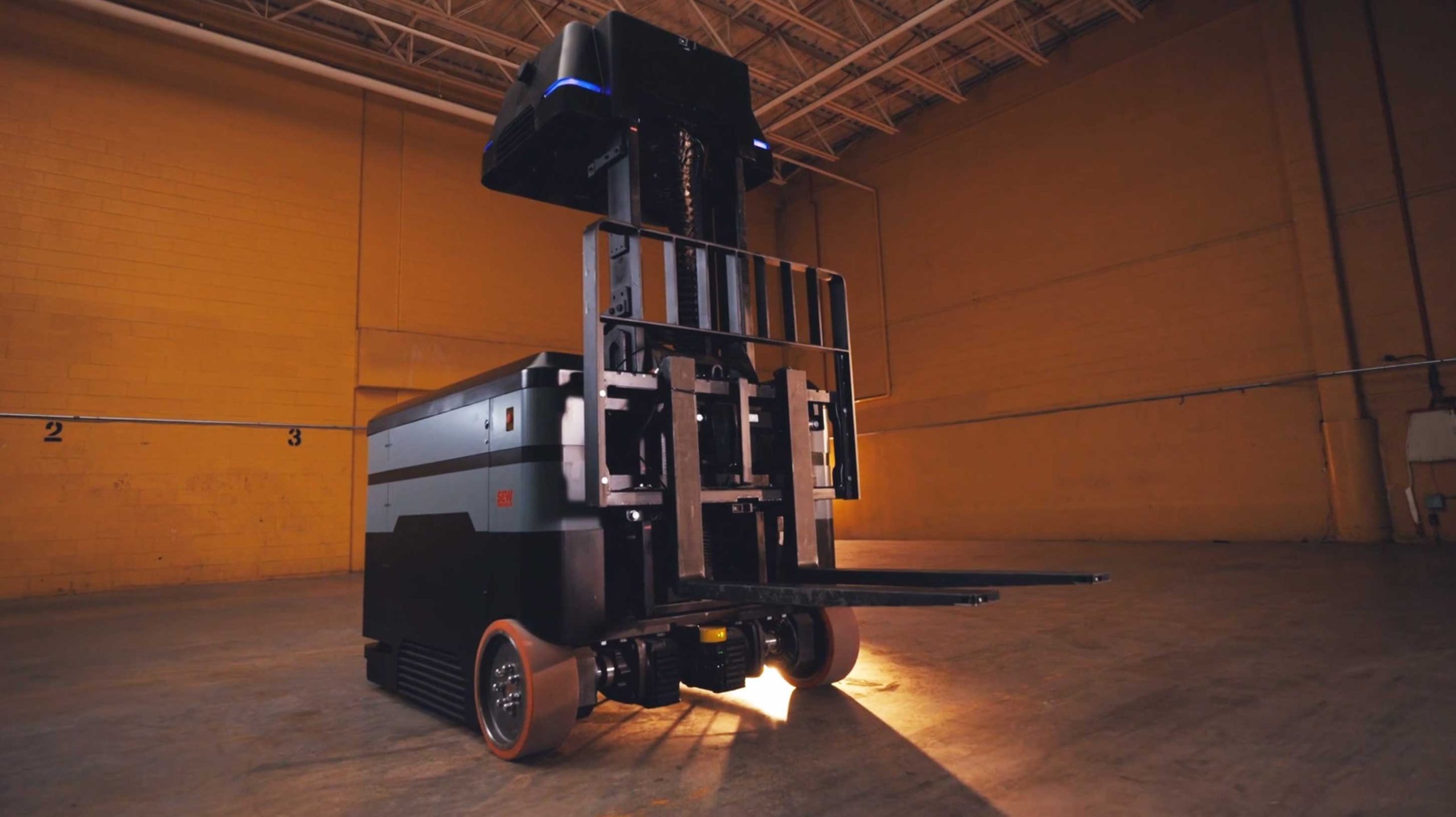 Autonomous robotic forklift with raised forks in a dimly lit warehouse.