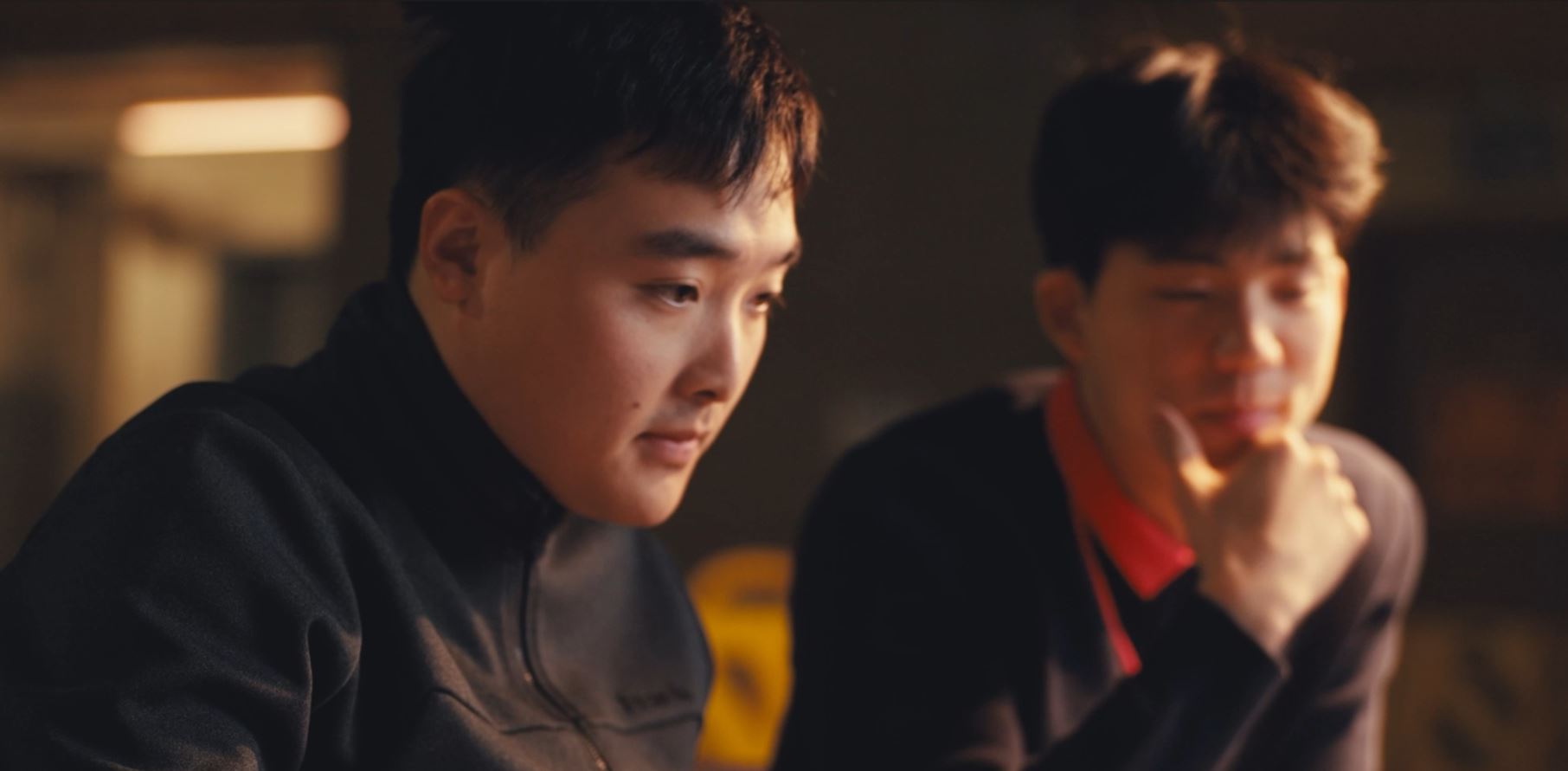 Two young men focused on a screen, working together in a dimly lit room.